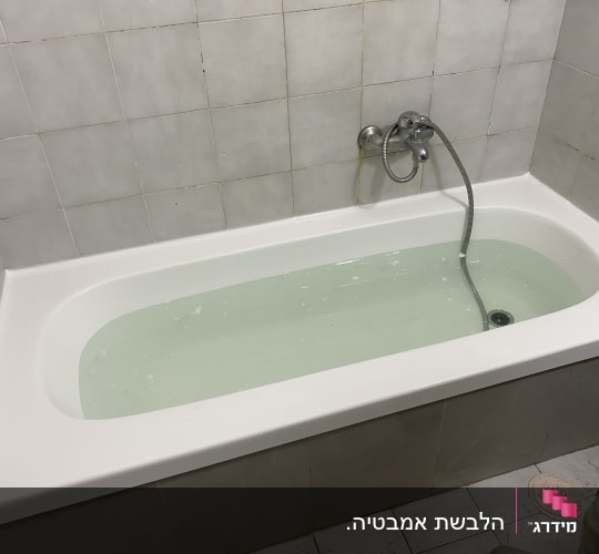 אמבטיה מלאה מים עם ברז ומקלחת יד